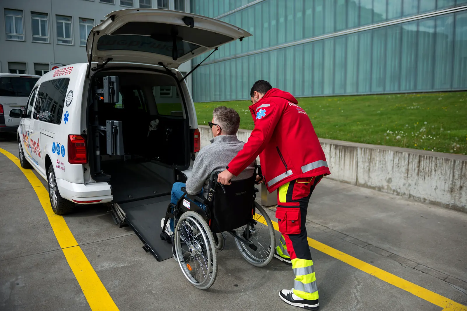 Mobimed-Mitarbeiter hilft einem Patienten im Rollstuhl über die Rampe ins Fahrzeug